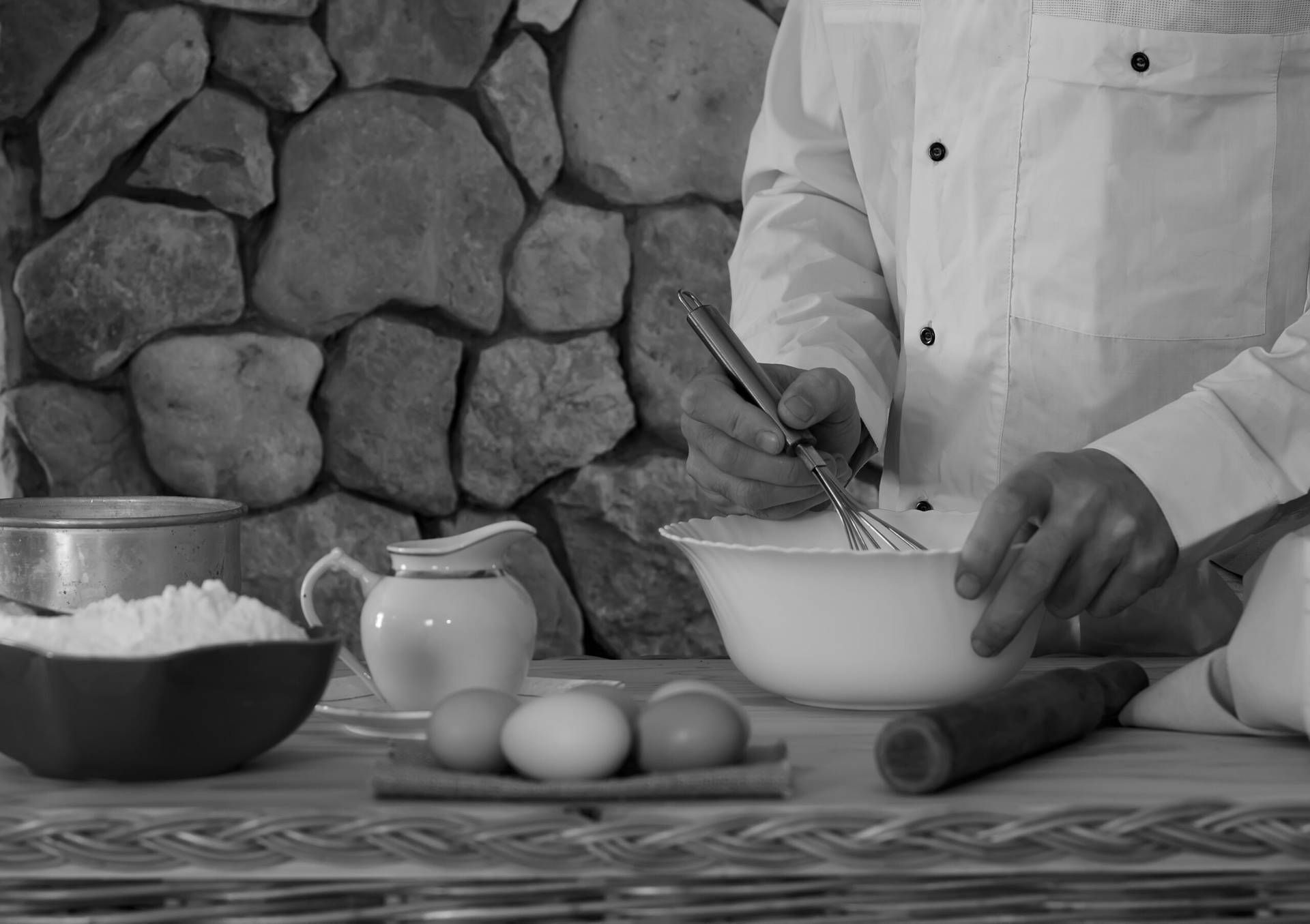 bowl with flour, eggs, a sieve and a mortar, and a male cook in a white garment whisk the whisk the batter. Concept of rustic kitchen, selective focus. Copy space. black and white photo