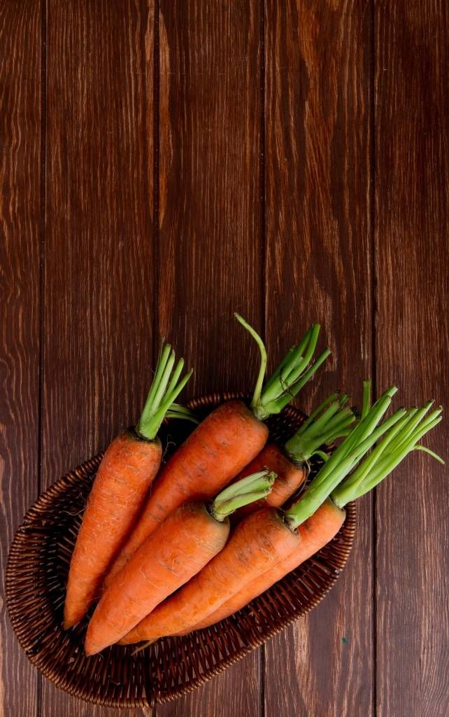 top view of basket plate with carrots on wooden background with copy space